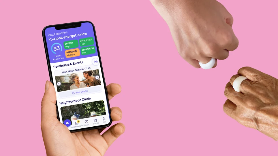 One hand holding a phone that shows the Comgrand app, with a health score, reminders and a neighbourhood circle, while a younger hand and an older hand each hold one of the rings.