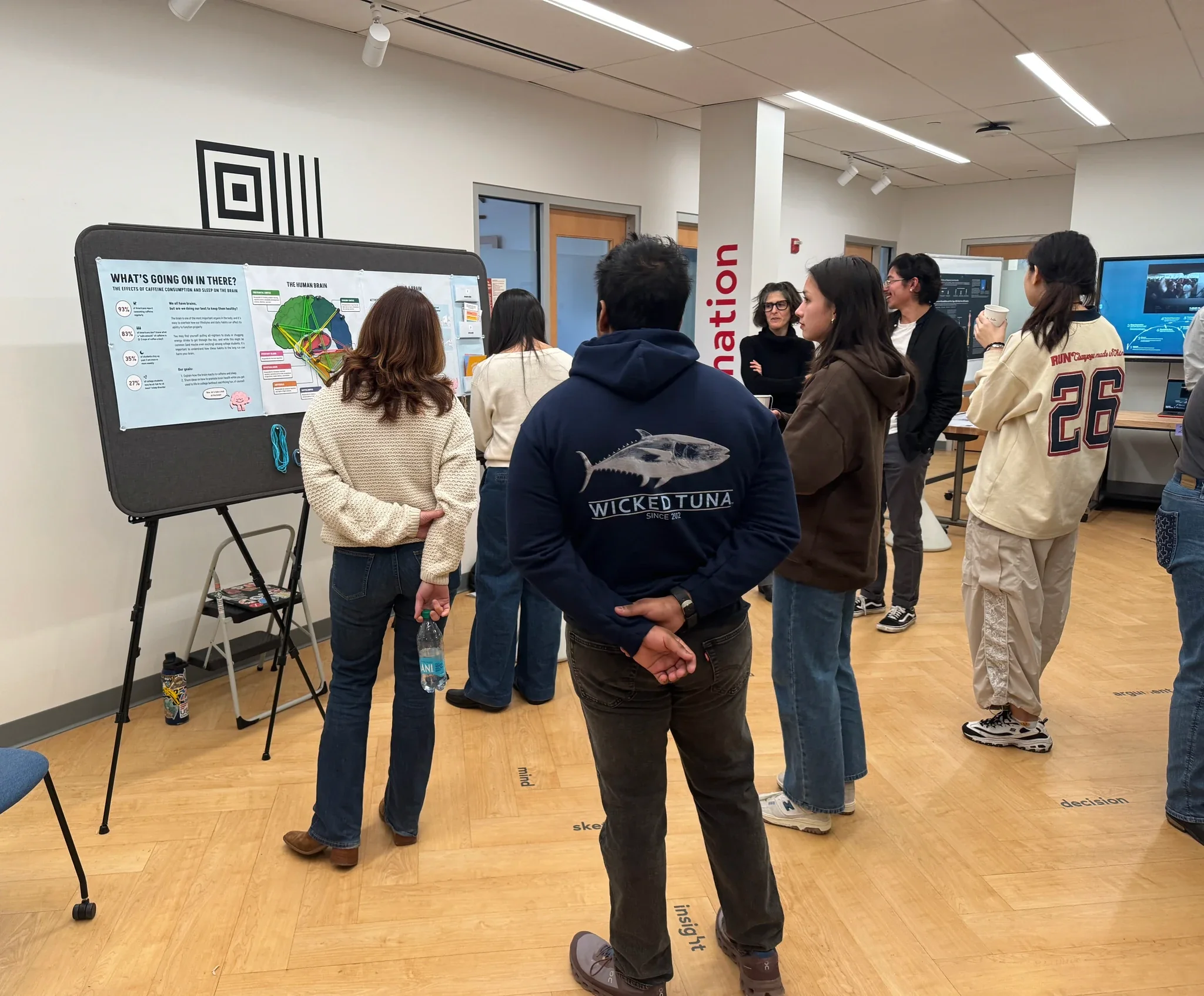 The exhibit installed on an easel in a gallery room, a printed brain panel with rubber bands hanging beside it, and seven visitors standing around it.
